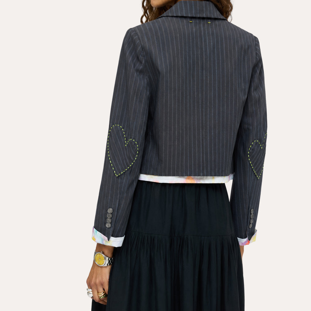 Close-up back detail of a navy pinstriped cropped blazer with yellow heart-stitched elbow patches and tie-dye cuff lining by Kerri Rosenthal