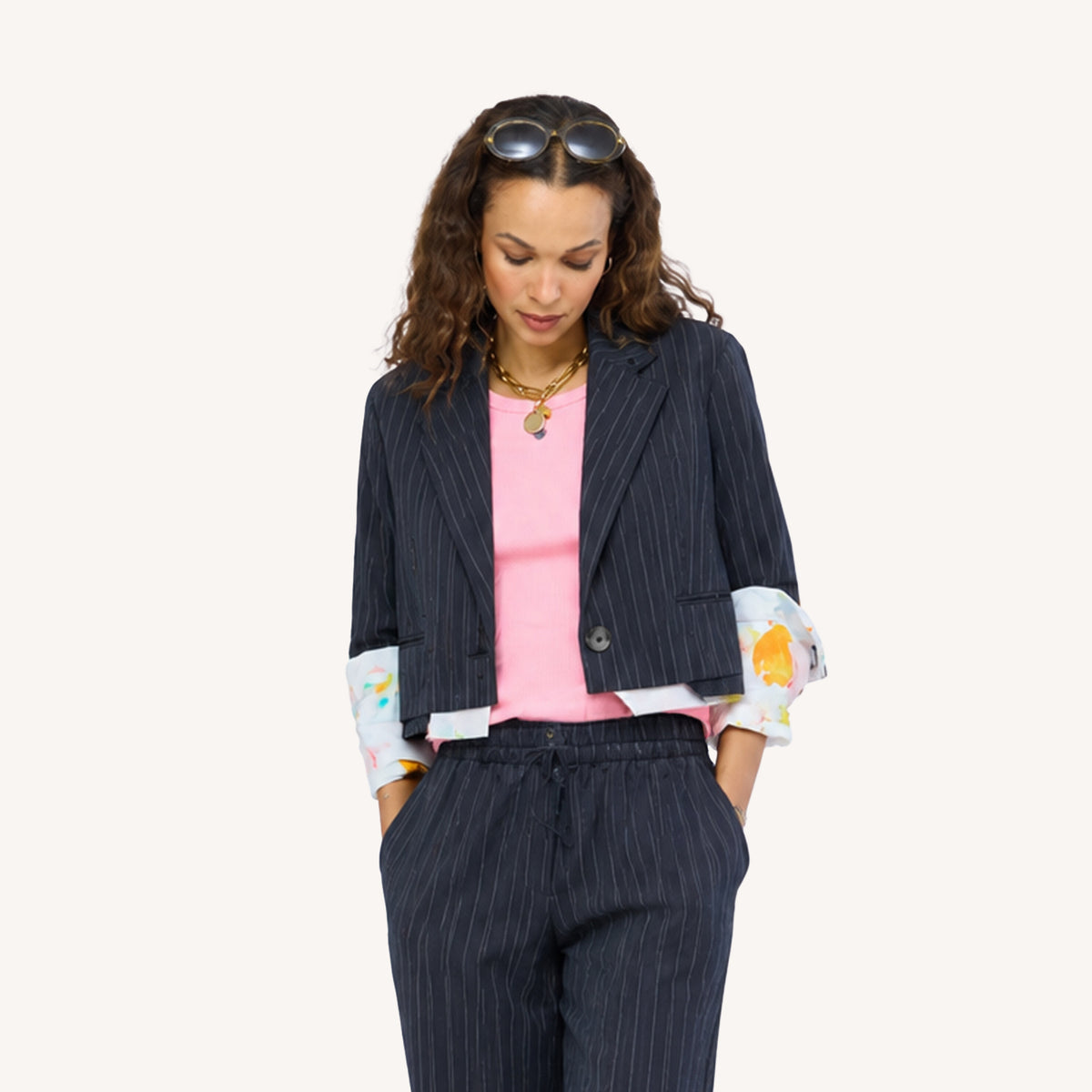 Close-up of Woman wearing a Kerri Rosenthal black pinstripe blazer and matching wide-leg drawstring pants with colorful art-print cuffs, styled with a pink top, gold chain necklace, and sunglasses on her head