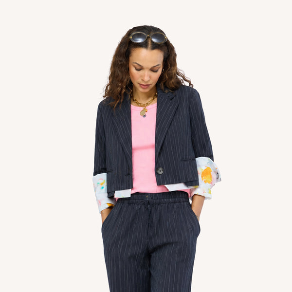Close-up of Woman wearing a Kerri Rosenthal black pinstripe blazer and matching wide-leg drawstring pants with colorful art-print cuffs, styled with a pink top, gold chain necklace, and sunglasses on her head