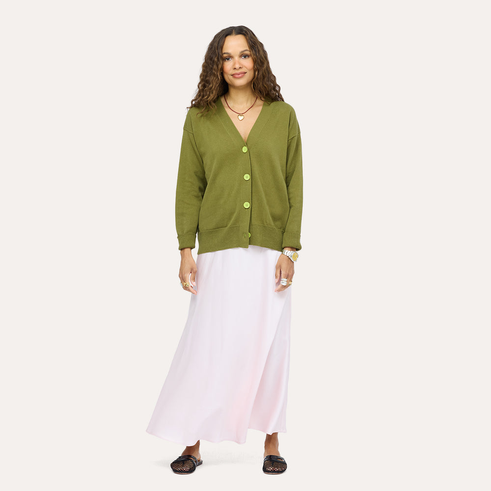Woman wearing a Kerri Rosenthal olive green v-neck knit cardigan with chartreuse buttons, styled with a blush pink maxi skirt and black woven loafers.