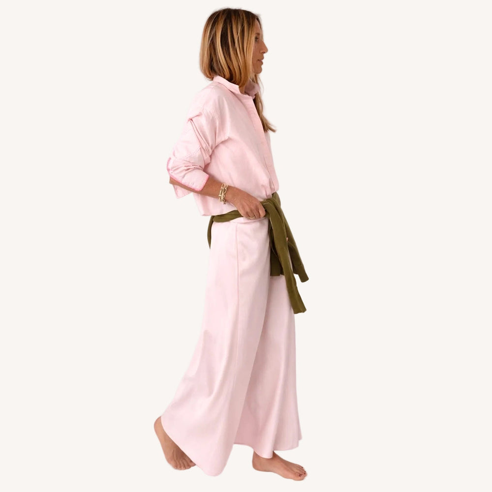 Side view of a model wearing a cropped pink button-down top with an olive green sweater tied at the waist over a flowy pink maxi skirt, barefoot