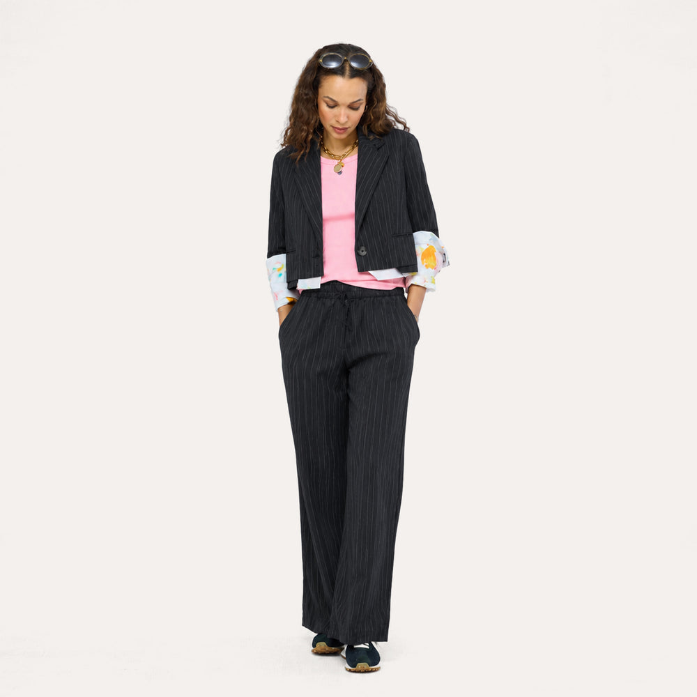 Woman wearing a black pinstripe blazer and pants with paint splat cuffs, a pink top, and sneakers.