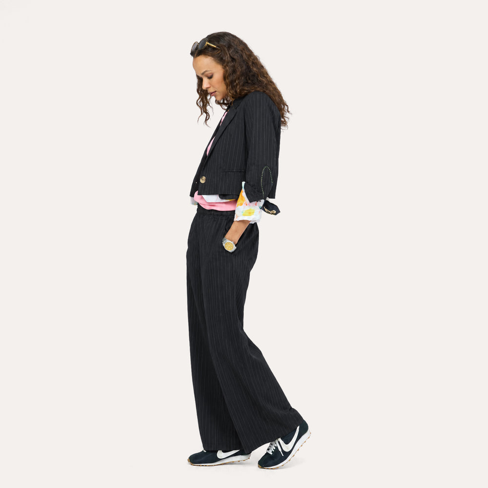 Side view of woman wearing a black pinstripe blazer and pants with paint splat cuffs, a pink top, and sneakers.