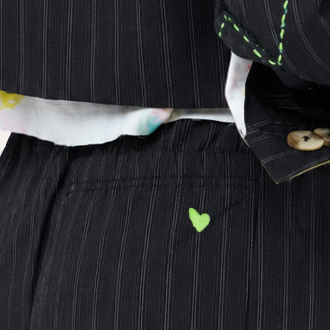 Close-up of black pinstripe blazer cuff and pants pocket detail, featuring colorful artwork lining and a neon green heart embroidery.