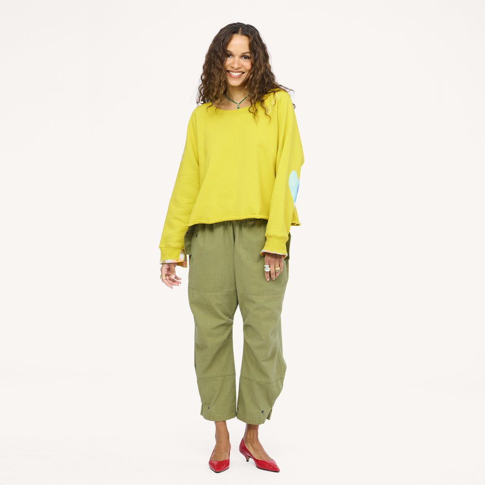 Woman wearing a chartreuse sweatshirt with a blue heart elbow patch, olive pants, and red heels.