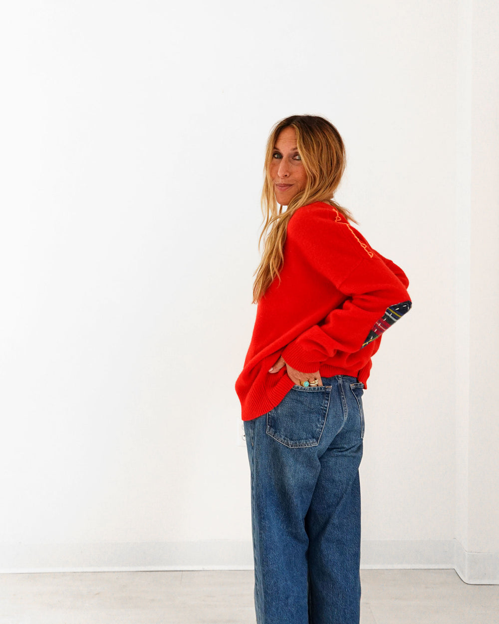 Kerri wearing the Frenchie Patchwork Sweater in red with jeans, hand on hip, side view