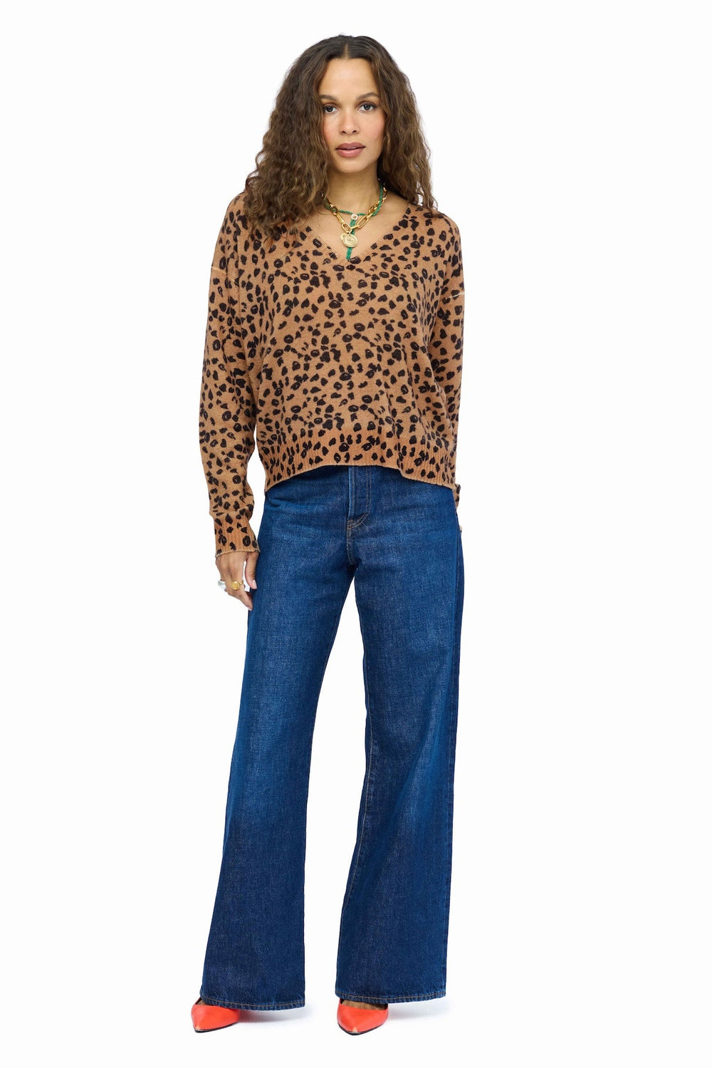 A woman modeling a brown and black leopard print long-sleeve V-neck top with blue jeans, set against a plain light gray background.