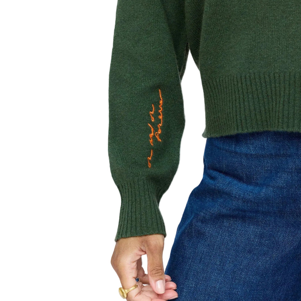 Close-up of "On and On Forever" hand-embroidered text in orange thread on the sleeve cuff of a green cashmere sweater