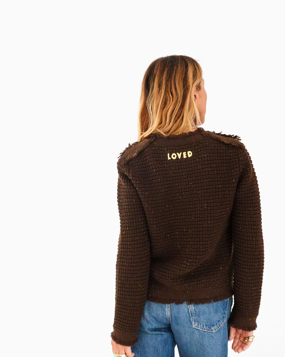 Kerri wearing the Fringe Beau-Lero Cardigan in cocoa heather with jeans, back view showing 'loved' embroidered at the upper back