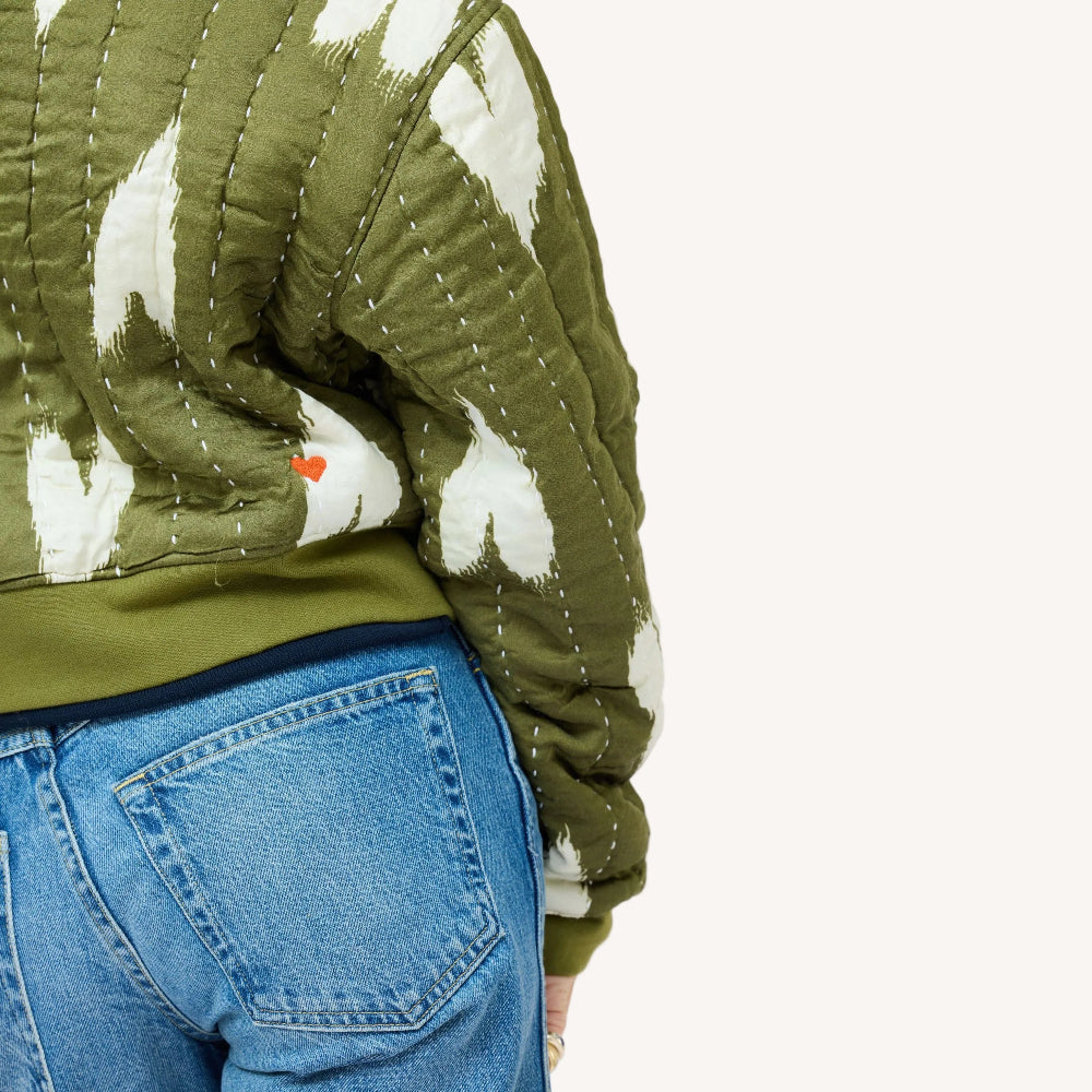 Close-up of woman wearing an olive green quilted bomber jacket with heart print, jeans. Shop jackets and blazers at Kerri Rosenthal.