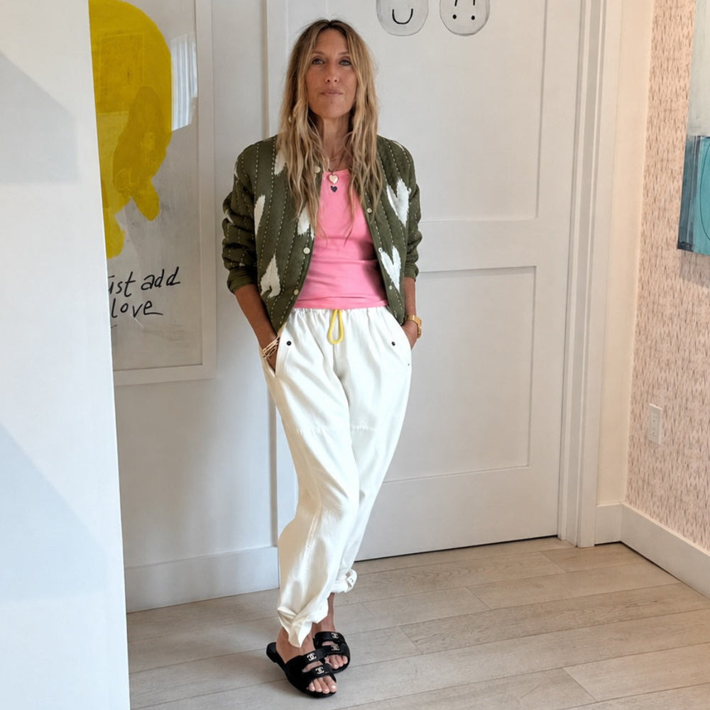 Woman wearing an olive green quilted bomber jacket with heart print, cream pant.