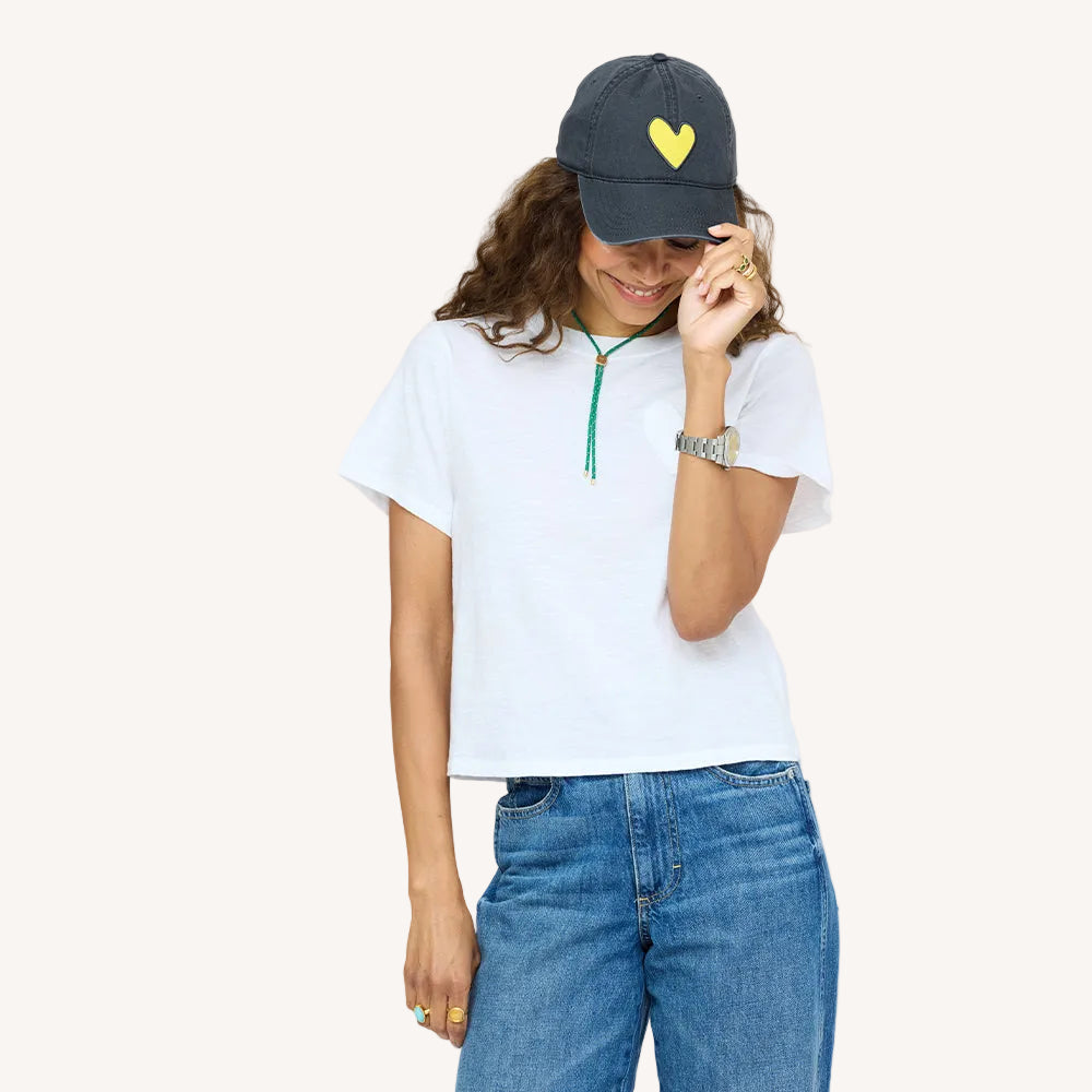 Woman wearing white tee, denim and  KR Imperfect heart coal baseball cap hat with yellow heart patch made from 100% cotton and adjustable strap - Shop heart baseball caps by Kerri Rosenthal