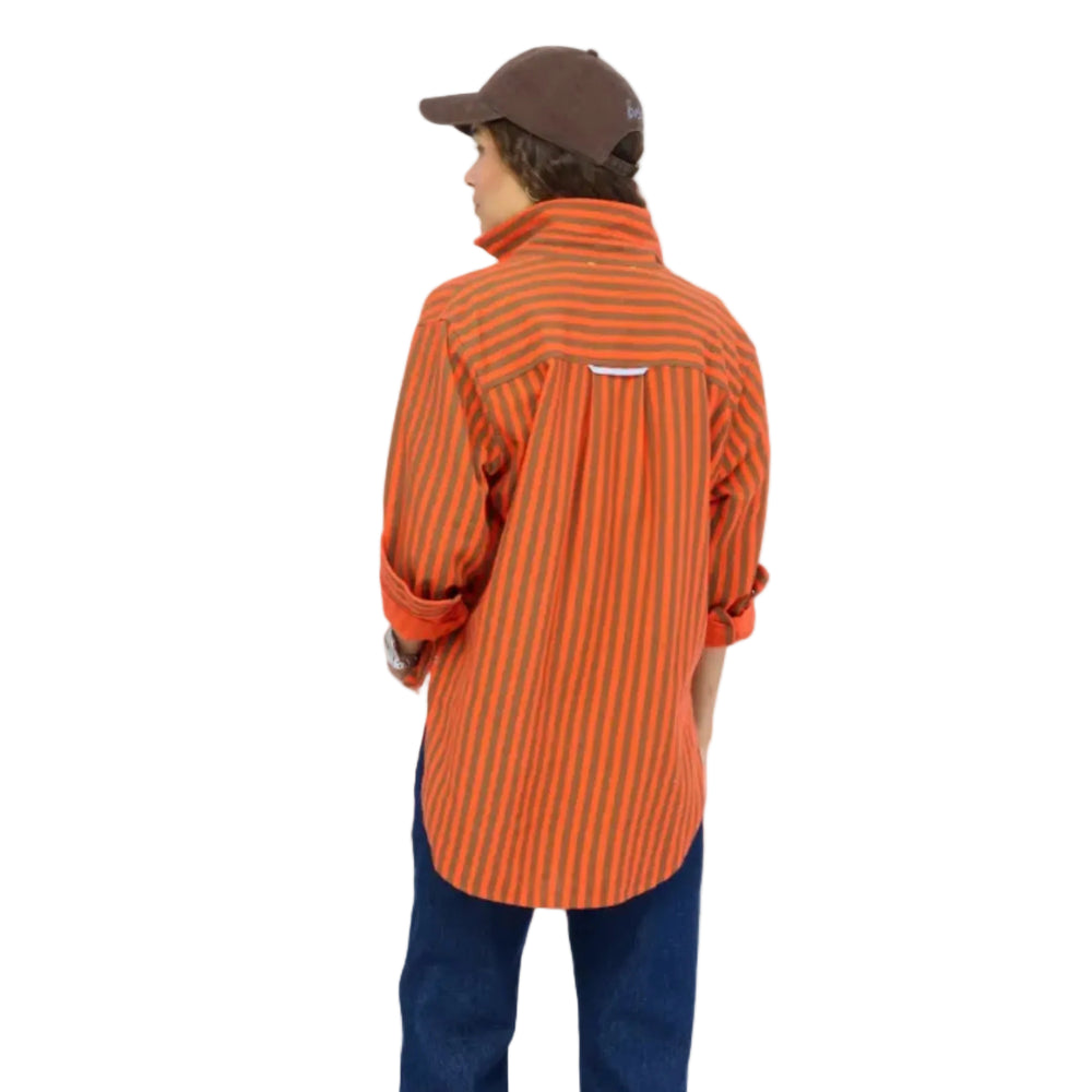 Back view of a woman wearing a Kerri Rosenthal orange and brown striped button-down shirt, dark denim jeans, a brown heart-graphic cap, and a wristwatch.