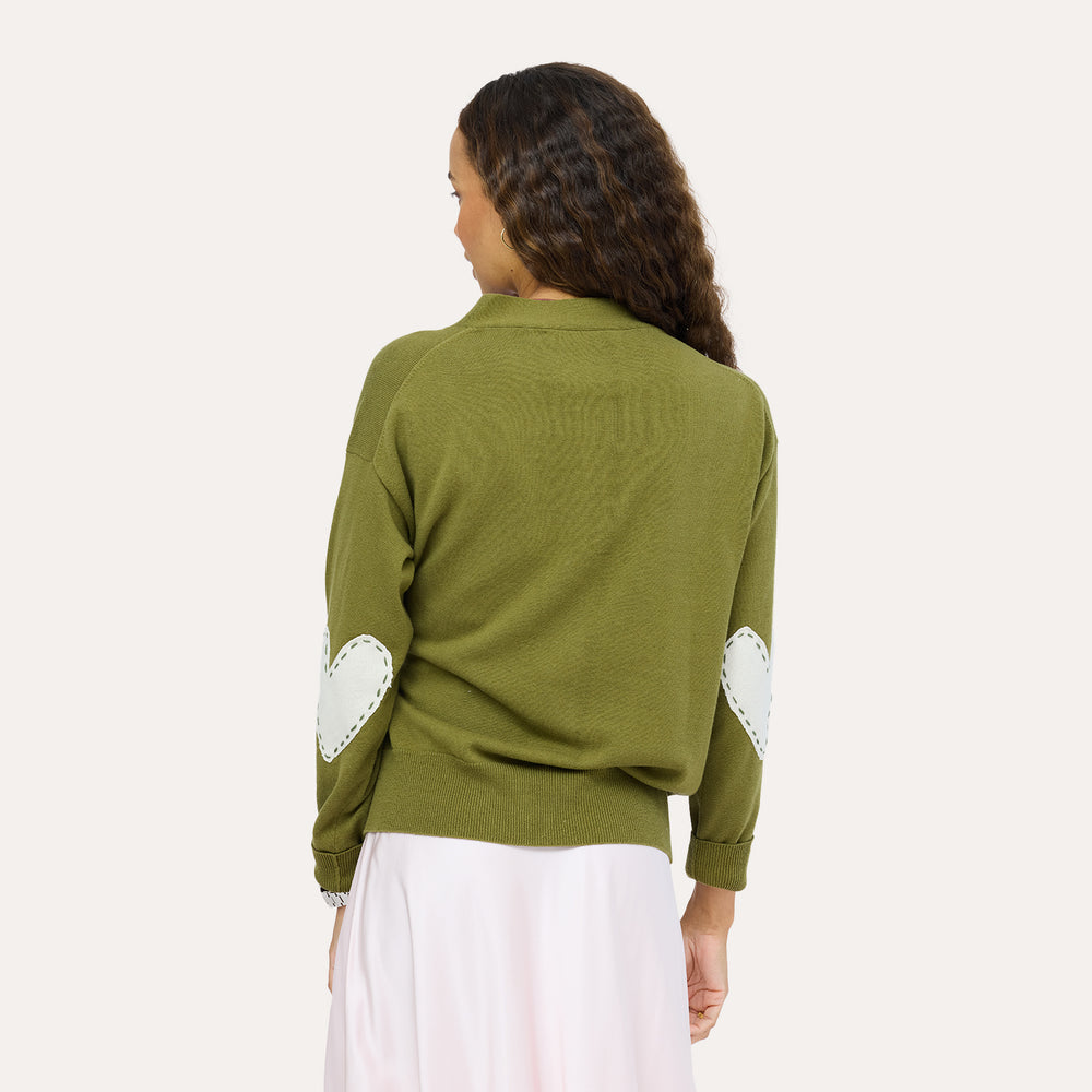 Back view of a woman wearing a Kerri Rosenthal olive green knit cardigan featuring mint green heart elbow patches, styled with a blush pink maxi skirt.