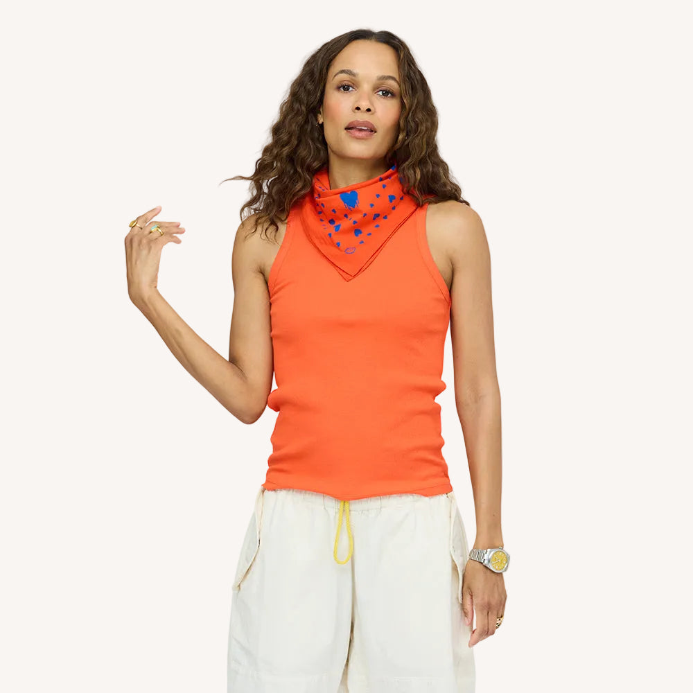 Woman wearing an orange tank top with a matching heart-print bandana scarf and cream drawstring pants.