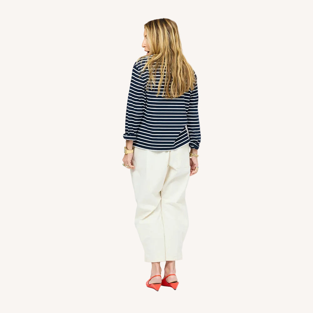 Back of woman wearing a Kerri Rosenthal navy and white striped long sleeve crewneck top styled with white pants and orange pointed toe flats.