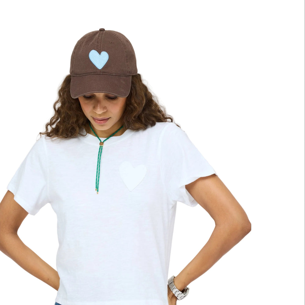 Kerri Rosenthal Imperfect Heart baseball cap in brown with blue chenille heart patch, front view on model with white tee