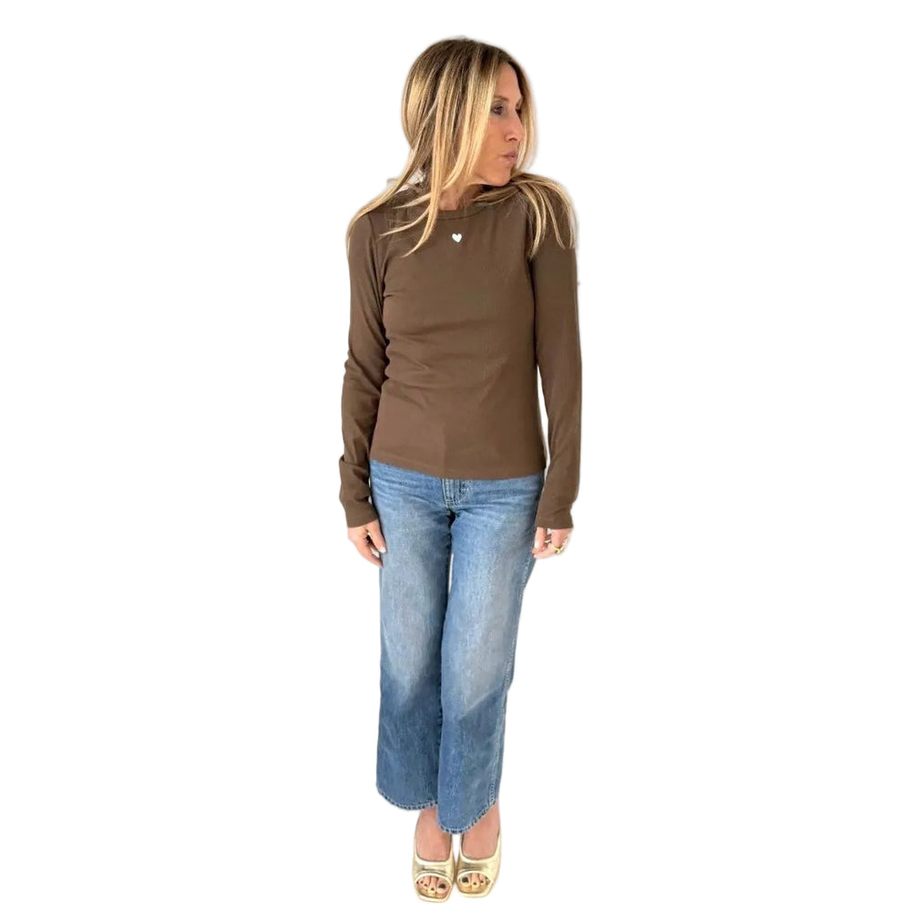 Woman wearing a brown long sleeve ribbed crewneck tee with hands raised in her hair, styled with wide leg denim jeans and platform sandals.