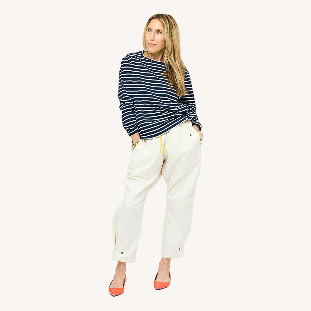 Woman wearing a Kerri Rosenthal navy and white striped long sleeve crewneck top styled with white drawstring pants with a yellow drawstring and orange pointed toe flats.