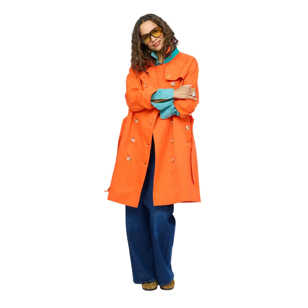 Woman wearing the KR Trench Coat in orange, a double-breasted colorful trench with teal contrast undercollar, styled with wide-leg denim jeans. Shop Kerri Rosenthal outerwear.