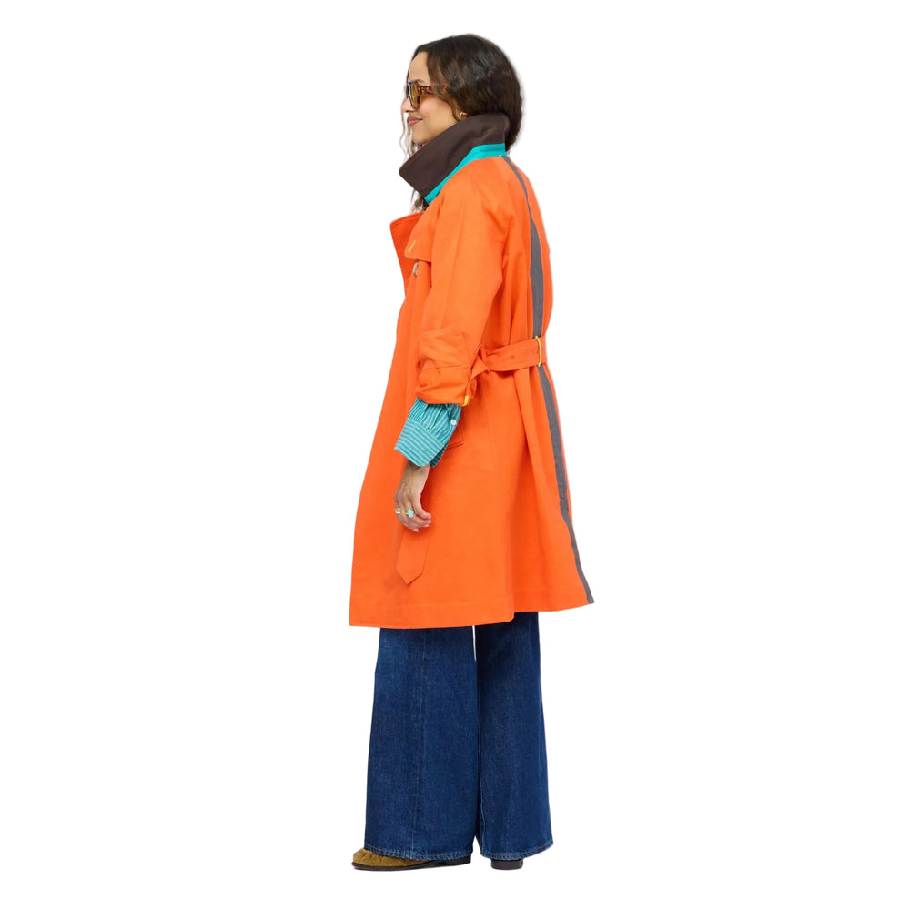 Side view of woman wearing the KR Trench Coat in orange, a double-breasted colorful trench with teal contrast undercollar, styled with wide-leg denim jeans. Shop Kerri Rosenthal outerwear.
