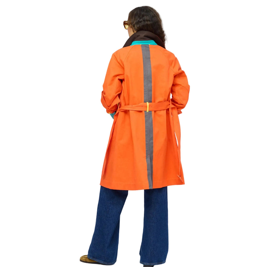 Back of woman wearing the KR Trench Coat in orange, a double-breasted colorful trench with teal contrast undercollar, styled with wide-leg denim jeans. Shop Kerri Rosenthal outerwear.