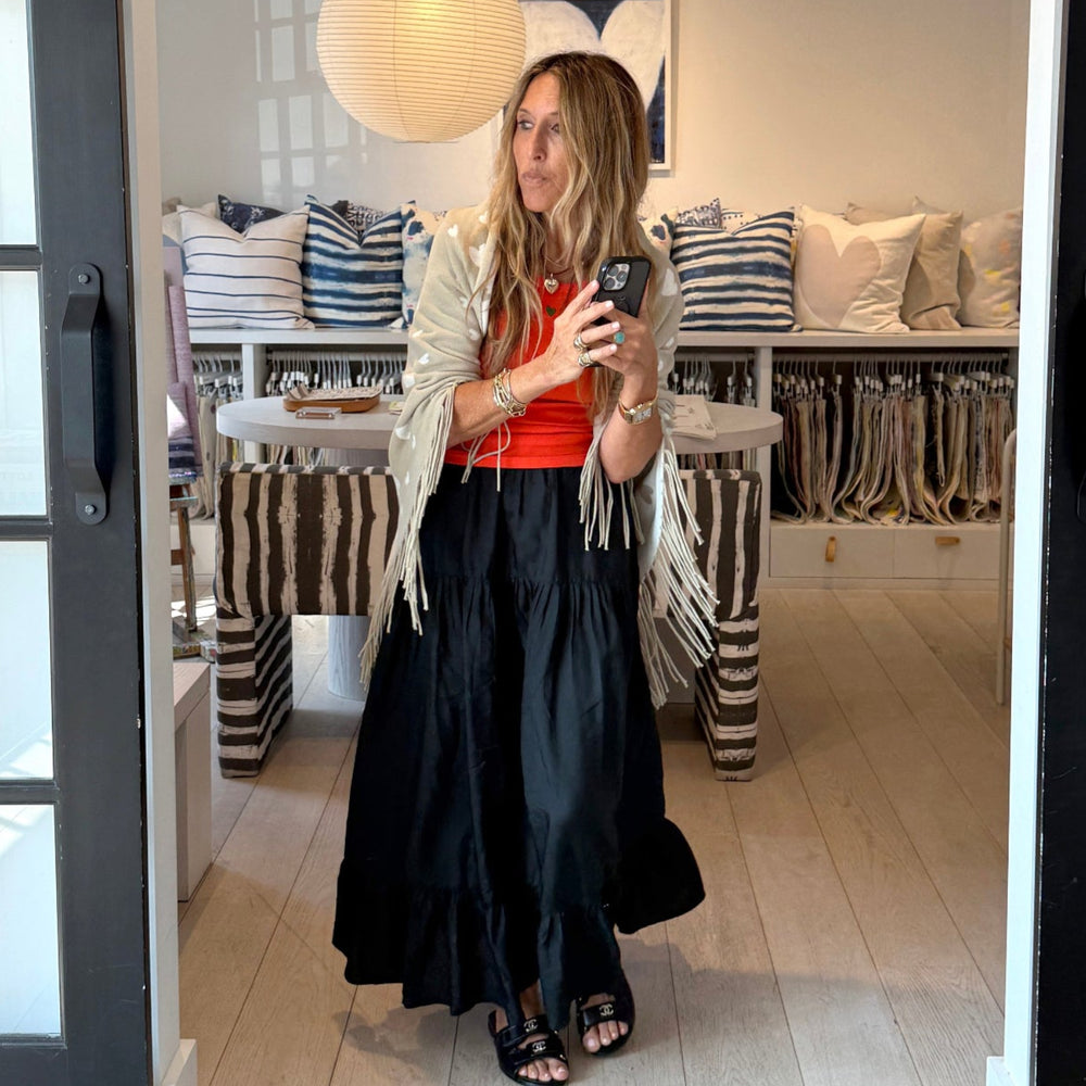 Model wearing a red-orange tank top with a sage green poncho and a black tiered maxi skirt. Women's clothing by Kerri Rosenthal