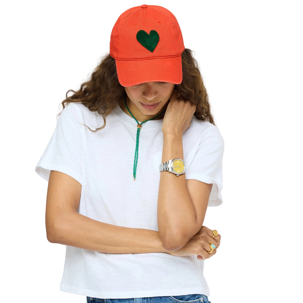 Model wearing Kerri Rosenthal Imperfect Heart baseball cap in orange with white tee and layered necklaces