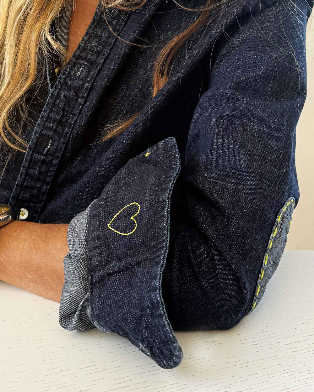 Close-up of shirt cuff embroidered with a small yellow heart, worn with the sleeve folded back.