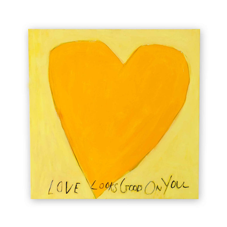 Oversized amber heart on soft butter-yellow canvas with the handwritten phrase LOVE LOOKS GOOD ON YOU in charcoal script below