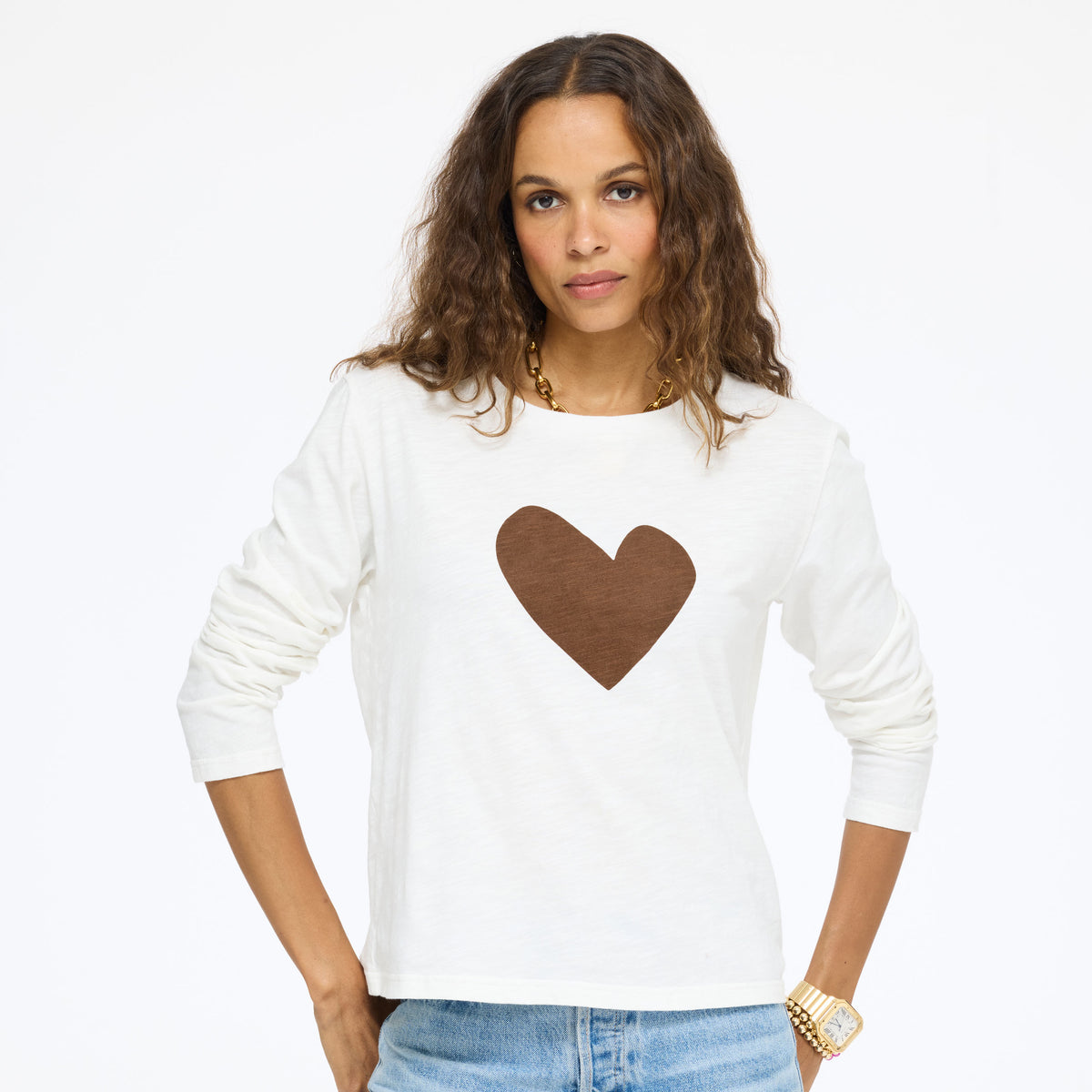 Model wearing the Long Sleeve Suke Imperfect Heart Tee in cream with a brown heart and jeans, hands in her pockets, front view