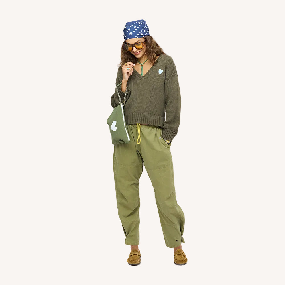 Woman wearing a green v-neck sweater with a blue drippy heart bandana, army green drawstring pants, and tan suede loafers.