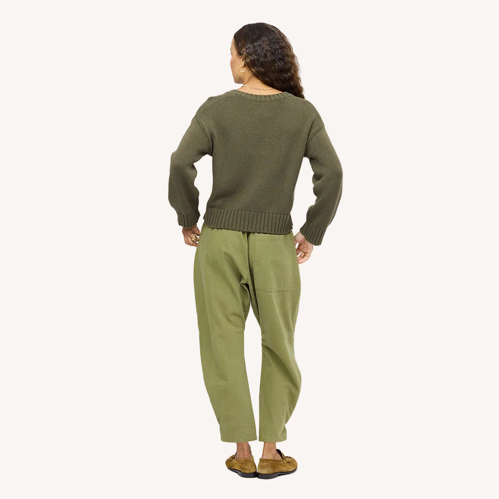 Back view of a woman wearing an olive green knit sweater, green pants, and tan suede loafers.