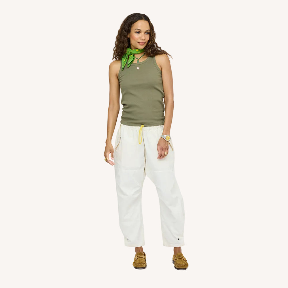 Woman wearing a green tank top with a green scarf, natural white drawstring pants, and tan suede loafers.
