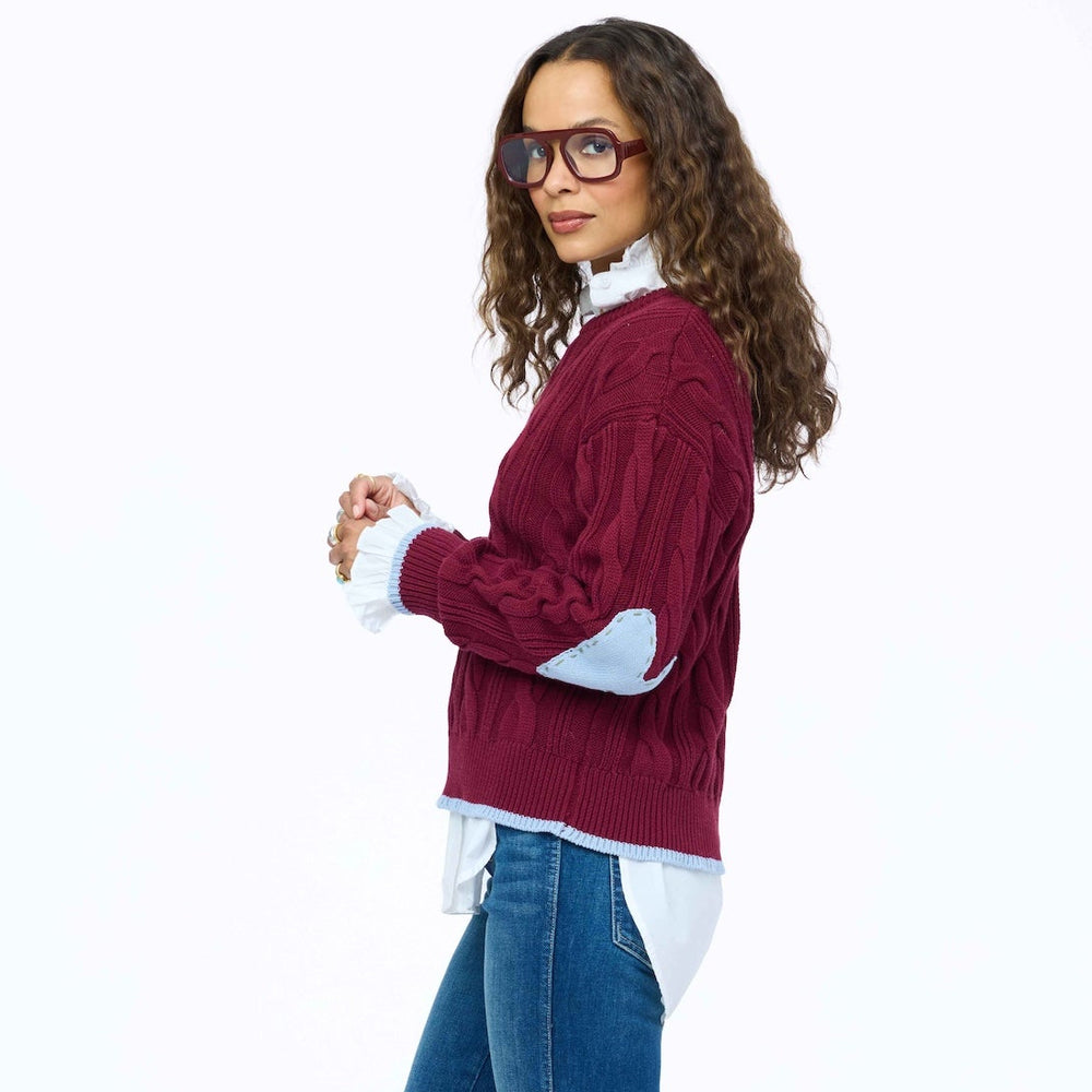 Kerri Rosenthal Maxwork Cable Pullover Sweater in Burgundy, woman standing in profile showing cable knit pattern and layered white shirt, styled with jeans and burgundy boots.