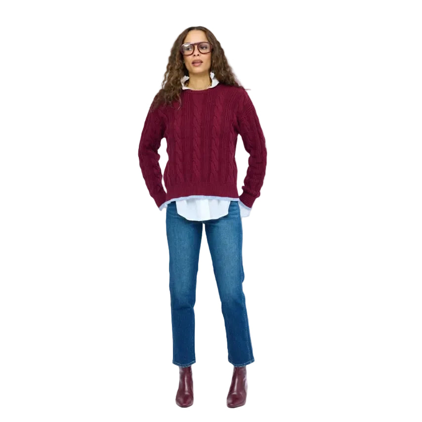 Kerri Rosenthal Maxwork Cable Pullover Sweater in Burgundy, woman standing showing cable knit pattern and contrast patchwork elbows, layered over a white shirt with jeans and burgundy boots.