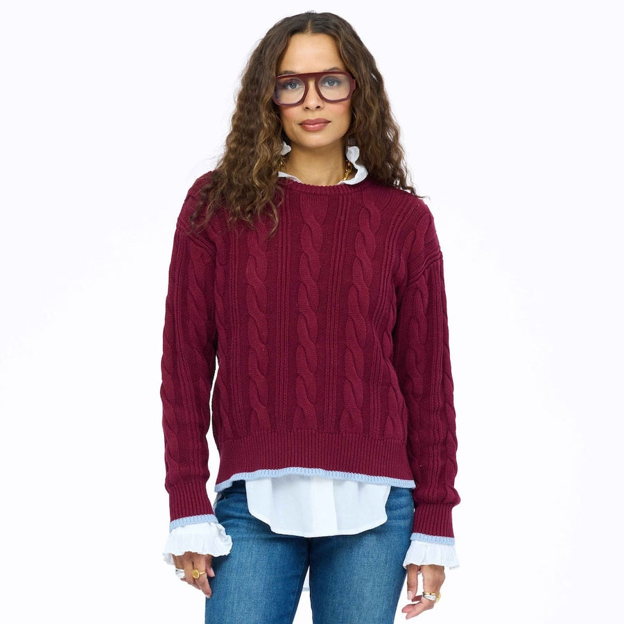 Kerri Rosenthal Maxwork Cable Pullover Sweater in Burgundy with contrast Imperfect Heart patchwork elbow patches, layered over a white poplin shirt with jeans.
