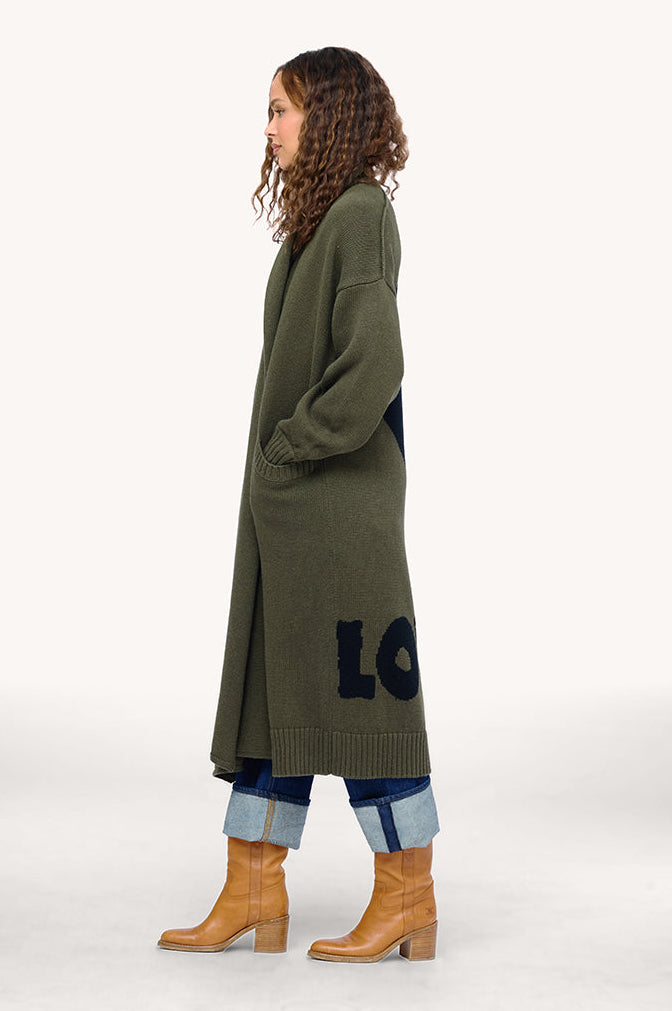 Model wearing Mercer Loved Duster in army green with black heart and "loved" design in back, side view.