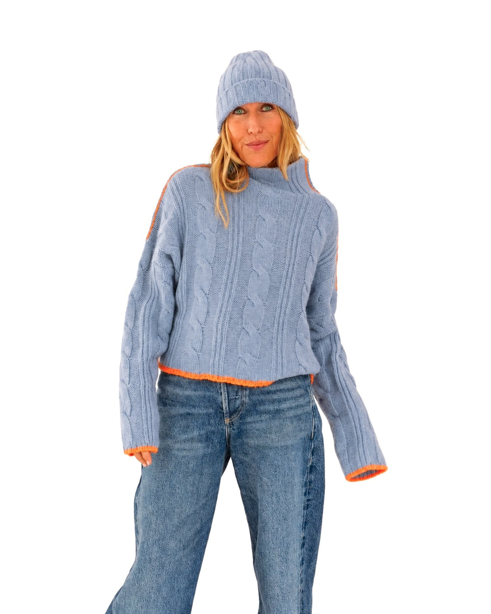 Kerri wearing the Hearth Sweater in blue with orange tipped cuffs and hem, the Winter Beanie in blue, and jeans, three-quarter view