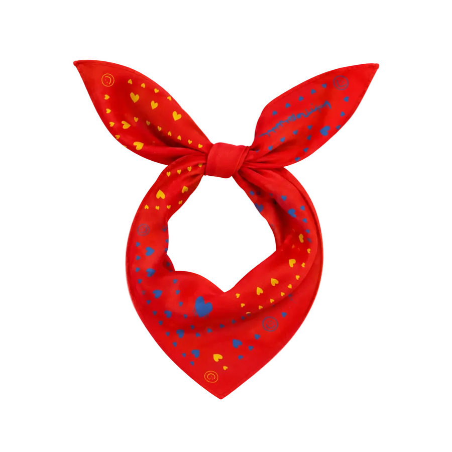 A red neck scarf tied in a bow, featuring a pattern of small yellow hearts, blue hearts, and blue script text, displayed on a solid white background.