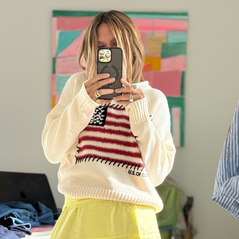 Woman wearing a cream sweater with an American flag design, and a yellow skirt, selfie. 