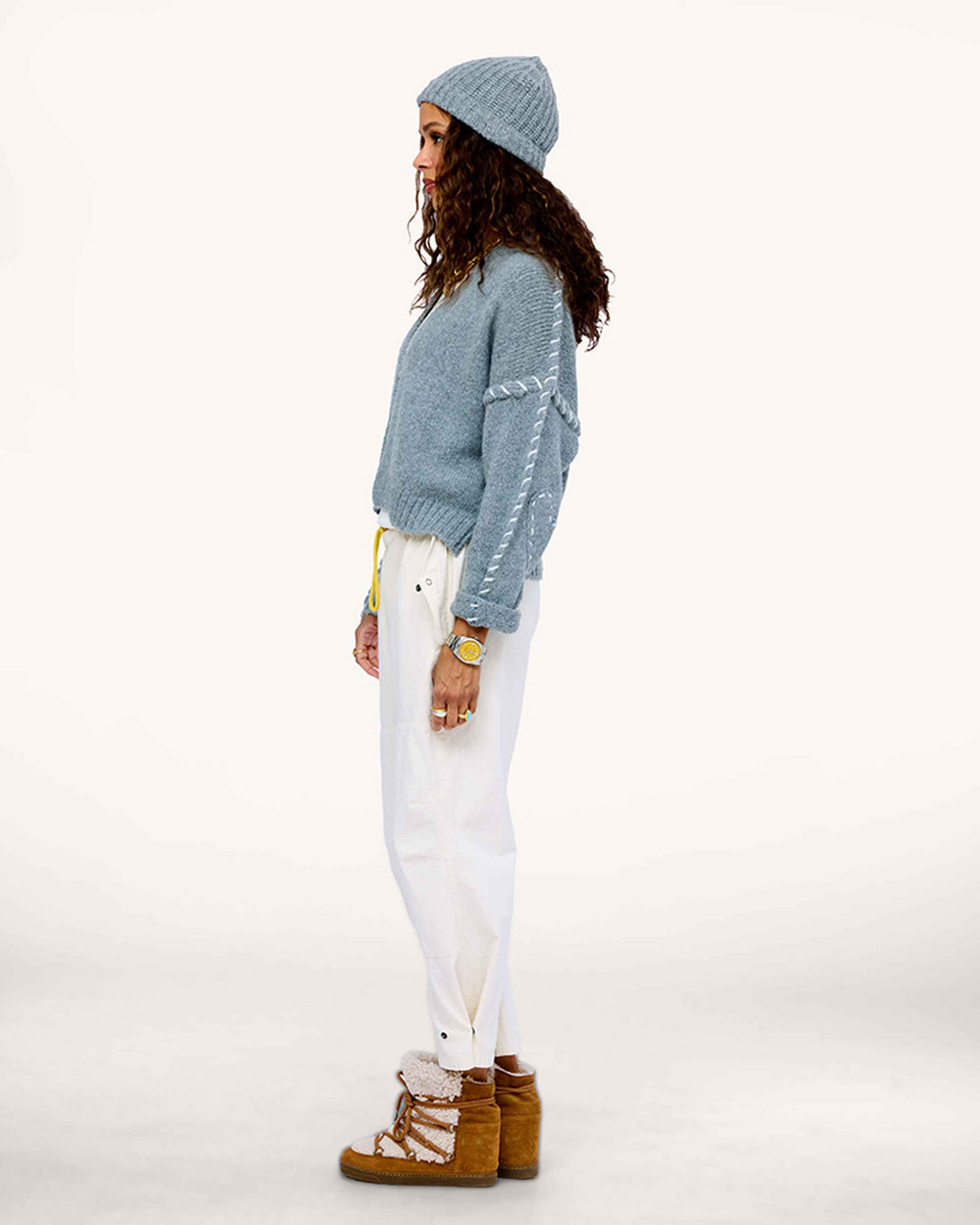 Model wearing Sienna Cardigan in Smoke gray, styled with light Love Brigade Pants and grey beanie, side view, showing off contrast stitching on sleeve and heart elbow patch.