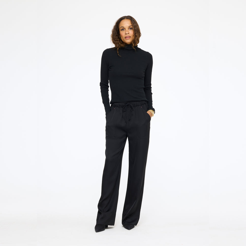 Model wearing the Coast Pant in black with a black mock neck top, full length front view