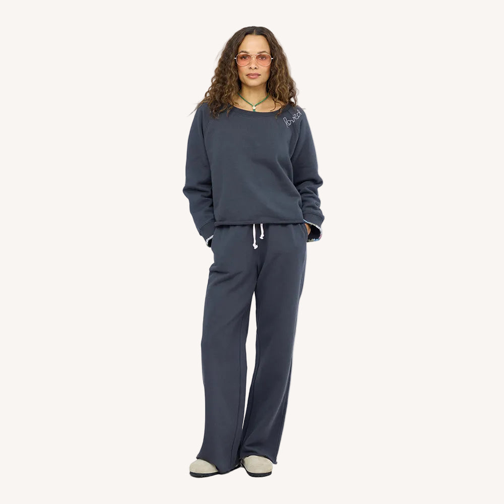 Woman wearing a charcoal sweatshirt with 'loved' embroidered on neckline and matching sweatpants and sunglasses.