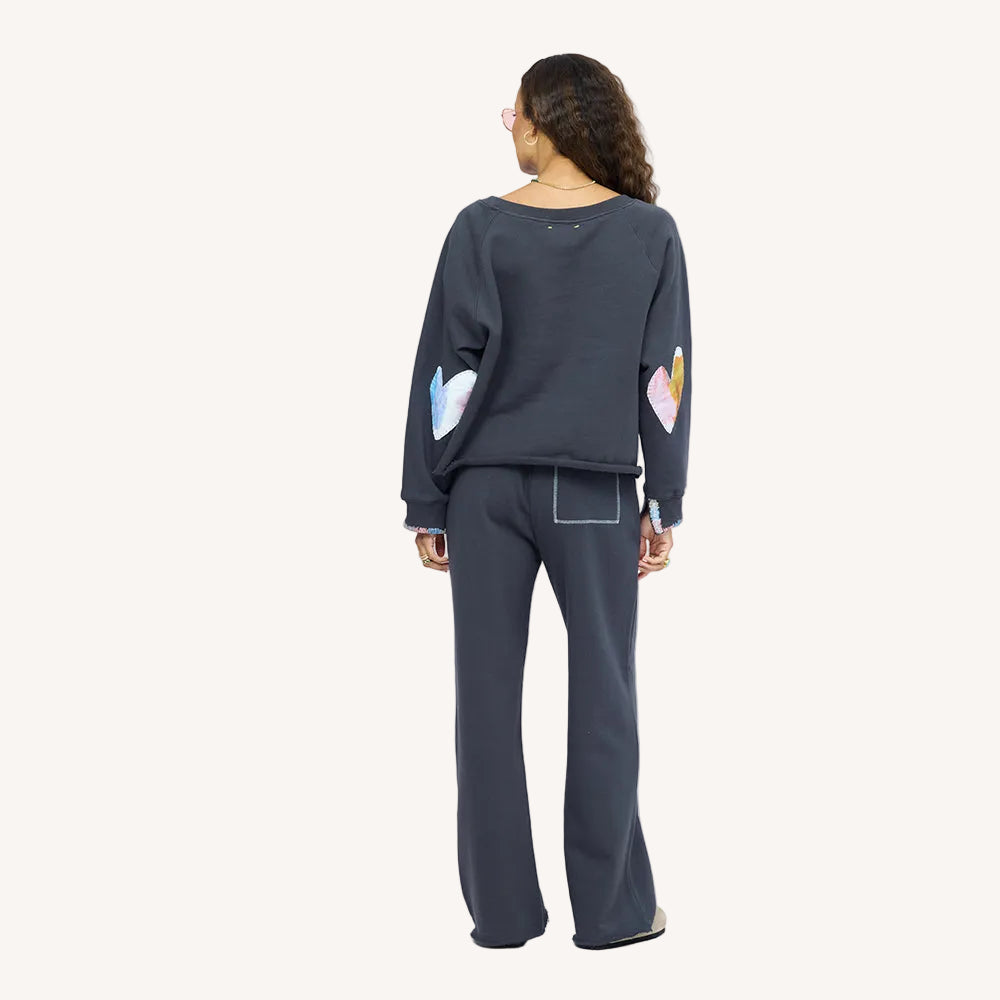 Back view of a woman wearing a charcoal sweatshirt with iridescent heart elbow patches and matching sweatpants.