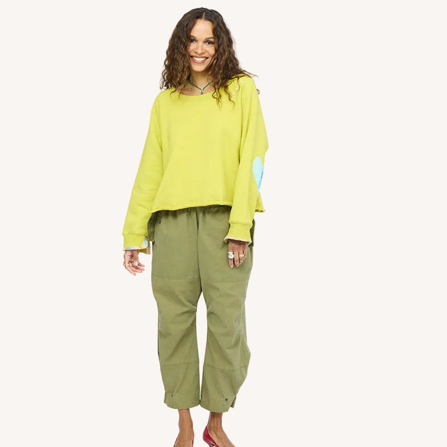 Woman wearing a chartreuse heart-patch sweatshirt with olive green pants and red heels.