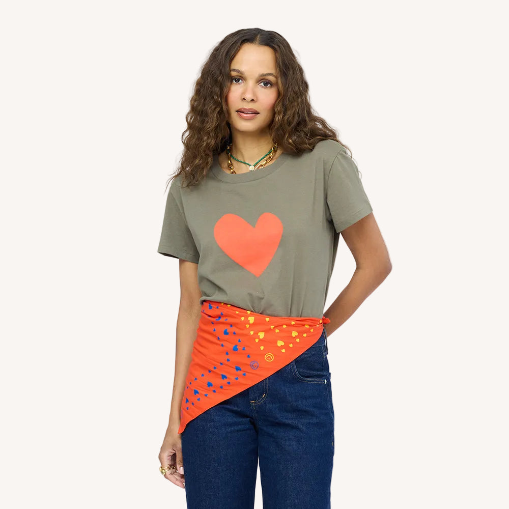 Woman wearing an olive green heart graphic t-shirt with an orange printed scarf tied at the waist, paired with dark wash denim jeans. Shop Kerri Rosenthal women's clothing.