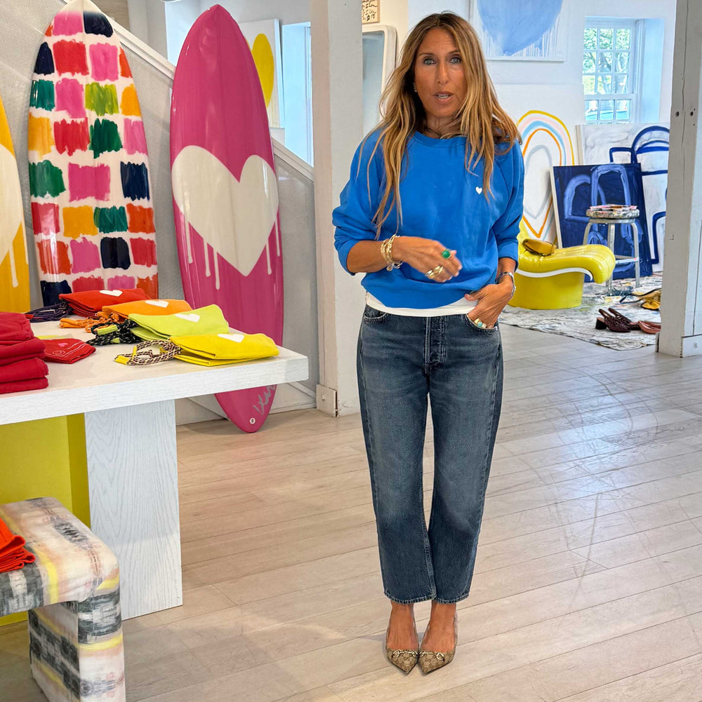 Woman wearing a blue crewneck sweatshirt with a small heart logo and jeans.