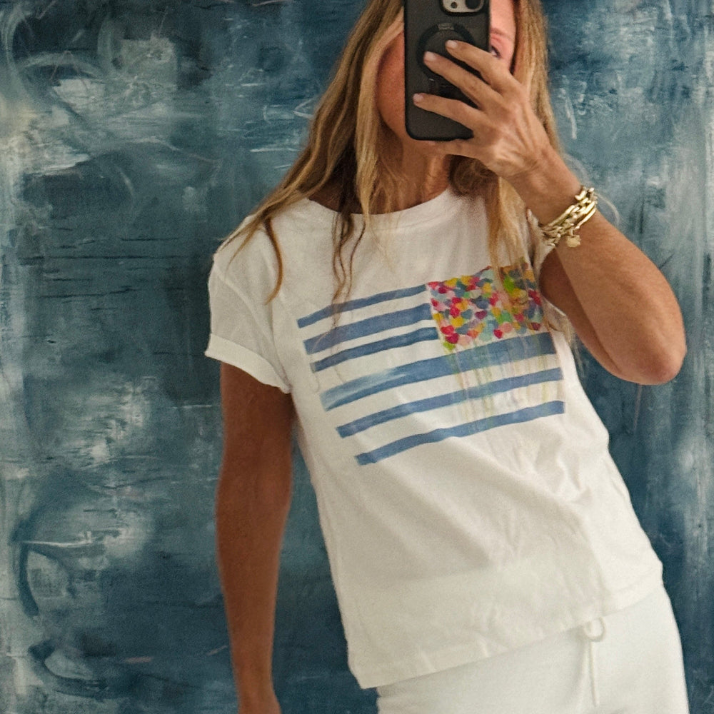 Person wearing a white t-shirt with blue stripes and a colorful graphic, standing against a textured blue wall.