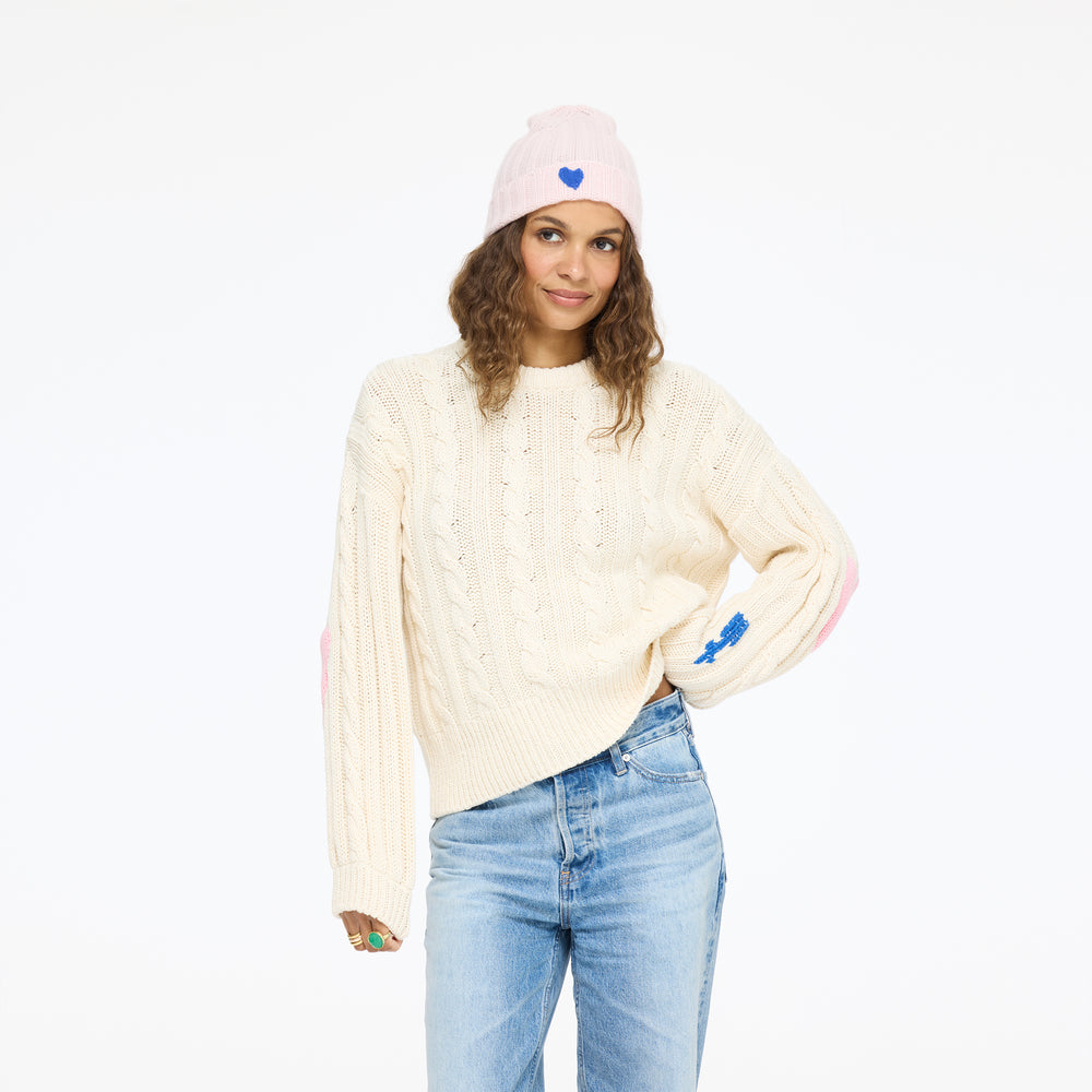 Model wearing the Rocky Patchwork Sweater in cream with the Winter Beanie in hardly pink and jeans, three-quarter view